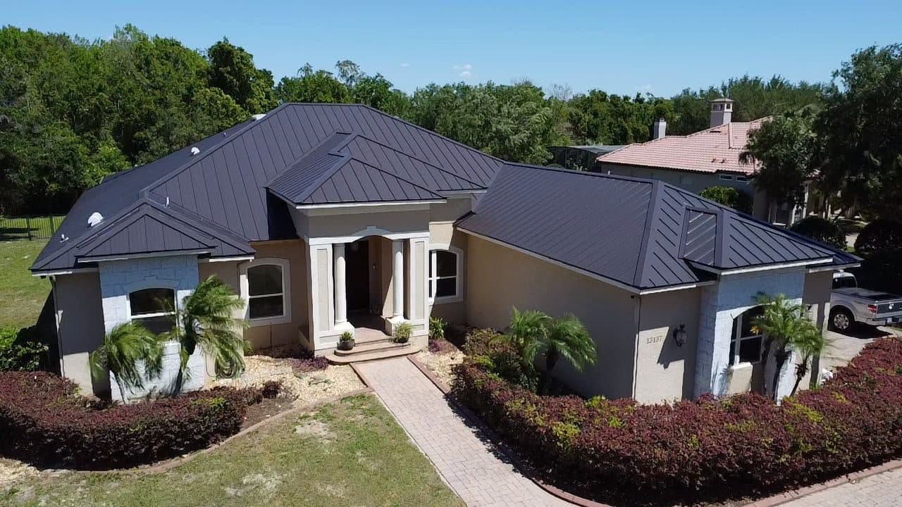 Completed dark standing-seam metal roof on a stucco home with a columned entry