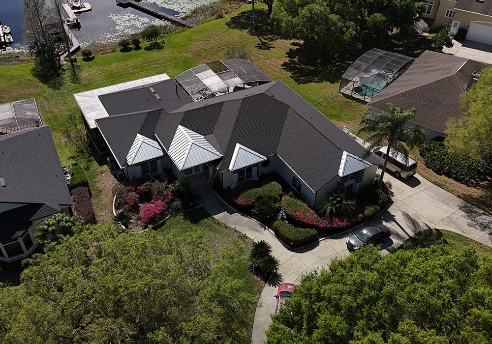 Aerial view of a charcoal shingle roof with multiple gables and flowering landscaping