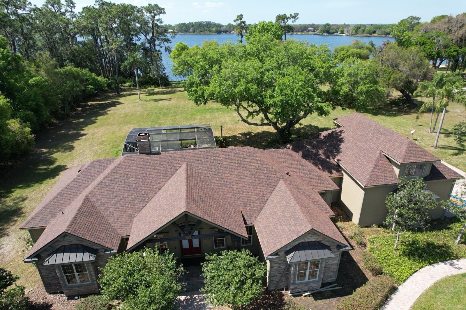 Aerial view of a completed shingle roof on a large lakefront home with dormers