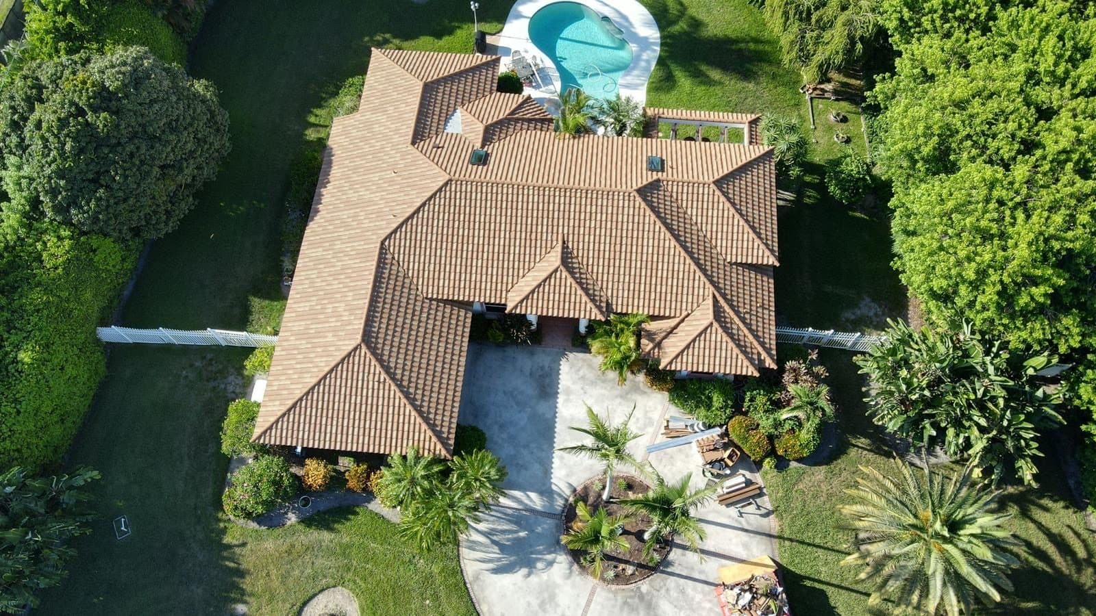 Aerial view of a completed barrel tile roof on a poolside Florida home surrounded by palms