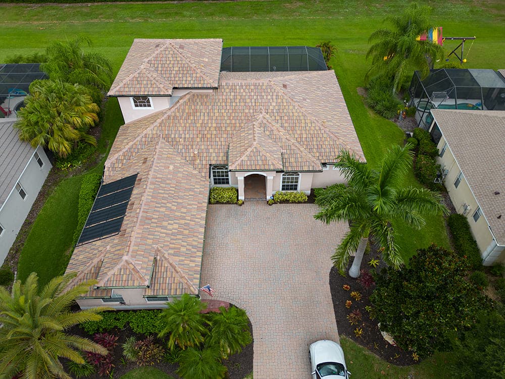 Aerial view of a blended tan flat-profile tile roof with roof-mounted solar panels and a paver driveway