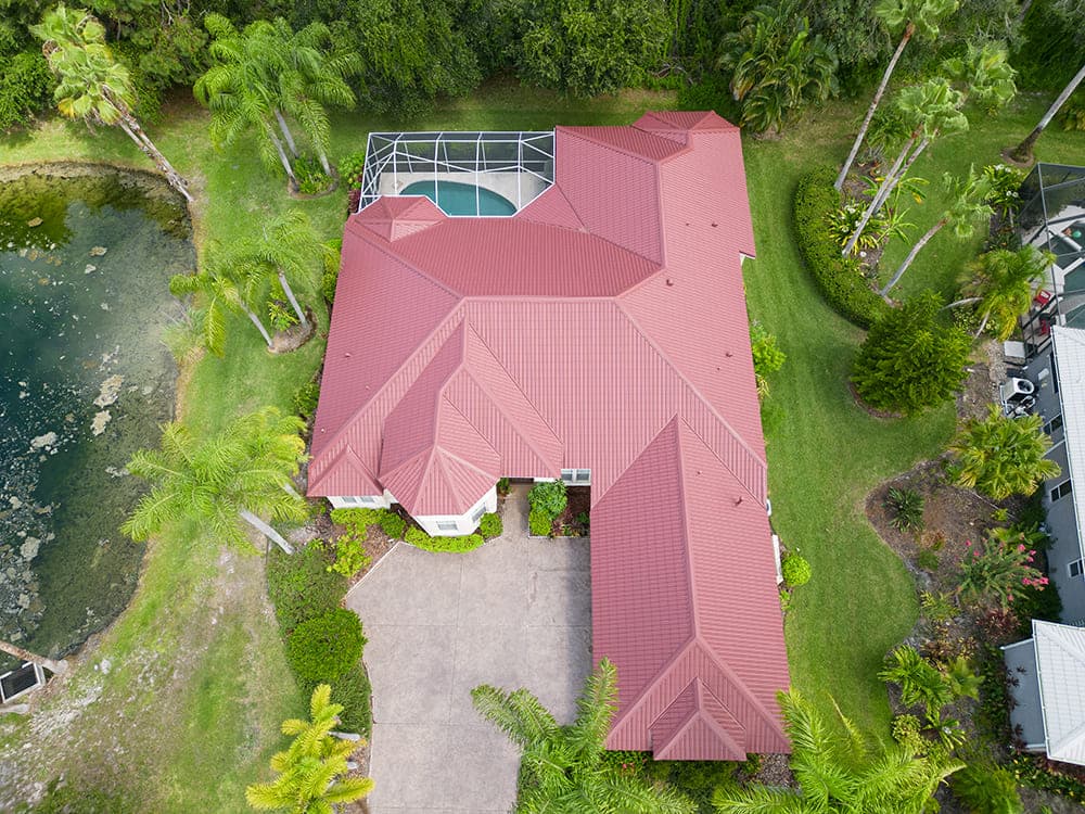 Aerial view of a red stone-coated metal roof in a tile profile, with mitred hips and a screened pool enclosure
