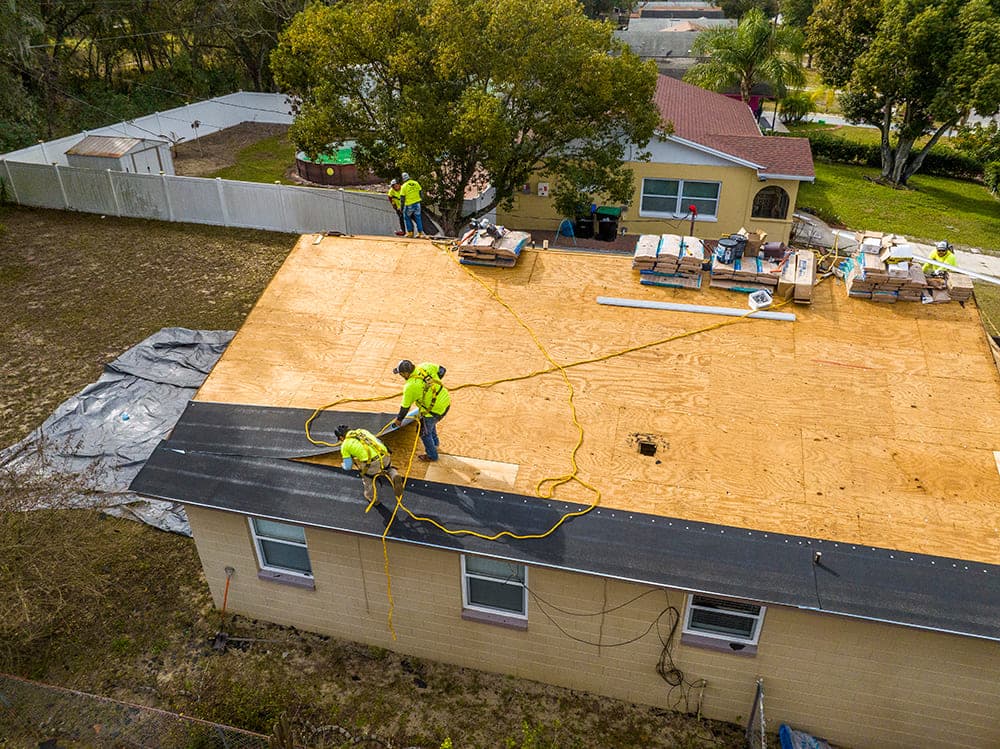 Aerial view of a crew working on exposed plywood decking during a full roof replacement