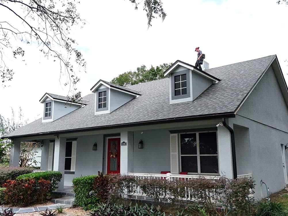 Roofer working along the ridge of a two-story home with dormers and a red front door