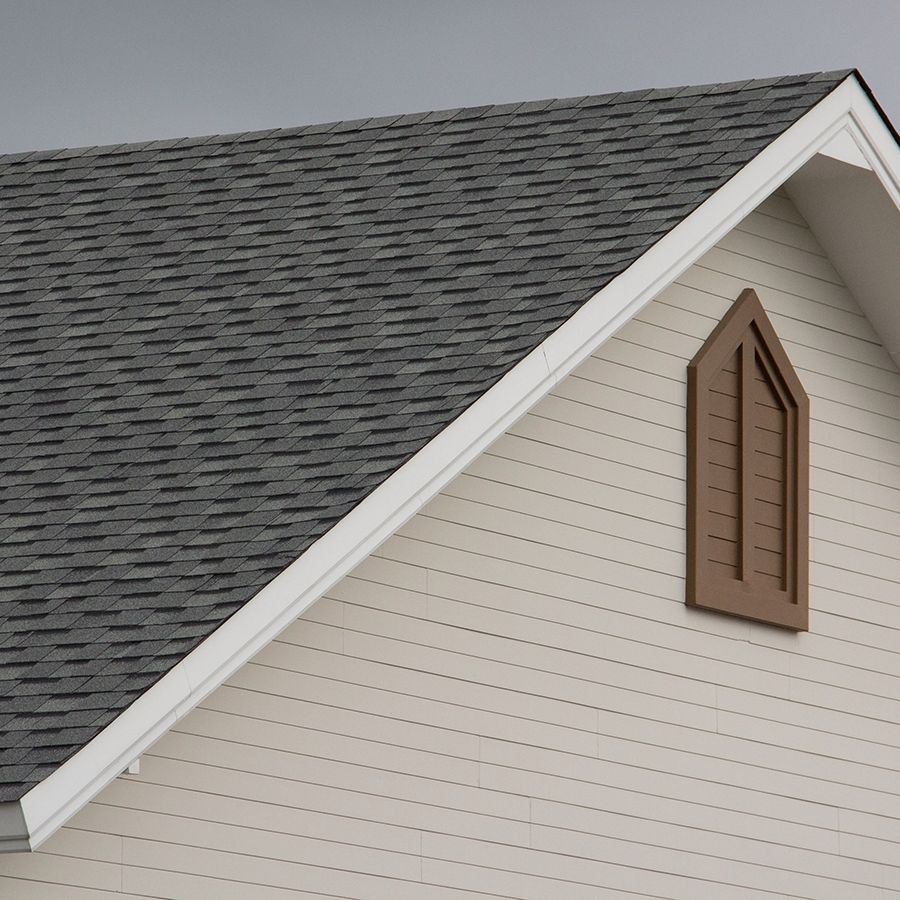 Zoomed in image of a roof on a residential home. Gray and cloudy skies behind home indicate a storm just hit or is about to hit.