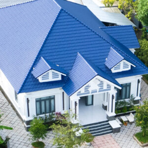 Aerial view of a modern house with a striking blue metal roof, featuring a spacious front porch, large windows, and well-maintained landscaping.