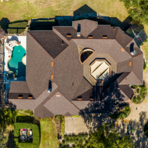 Aerial view of a residential neighborhood with a newly installed brown shingle roof, showcasing a house with a pool and well-maintained landscaping.
