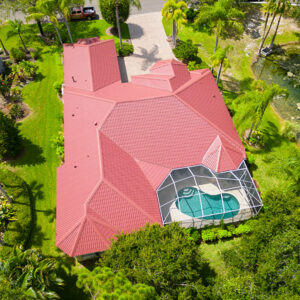 Aerial view of a residential neighborhood with a newly installed metal red roof, showcasing a house with a screened-in pool and well-maintained landscaping.