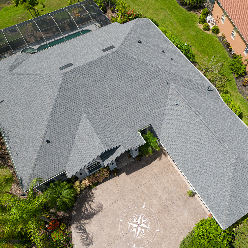 Aerial view of a beautiful home with a red metal roof surrounded by lush greenery and palm trees, highlighting the stunning residential roofing work. Ideal for showcasing quality home improvement and roofing services in a tropical setting.