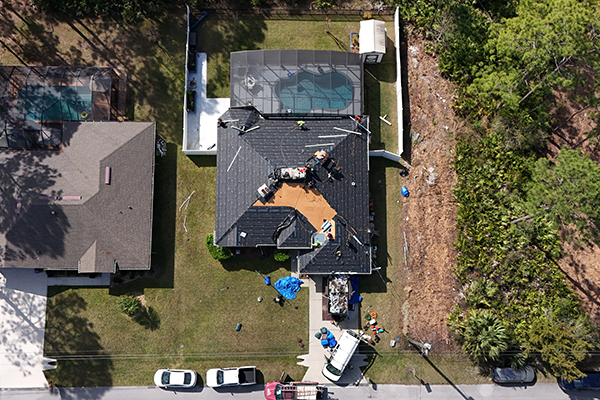 Aerial view of Noland's Roofing crew performing a residential roof replacement in Orange City, Florida, showcasing professional roofing installation with black shingles and active job site setup.
