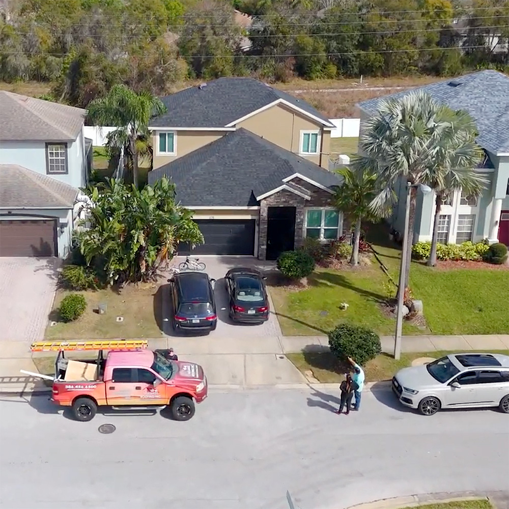 A Noland’s Roofing service truck parked outside a Florida home with a new shingle roof, as homeowners speak with a roofing team member after a completed project.