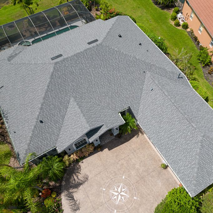 Aerial view of a beautiful home with a red metal roof surrounded by lush greenery and palm trees, highlighting the stunning residential roofing work. Ideal for showcasing quality home improvement and roofing services in a tropical setting.