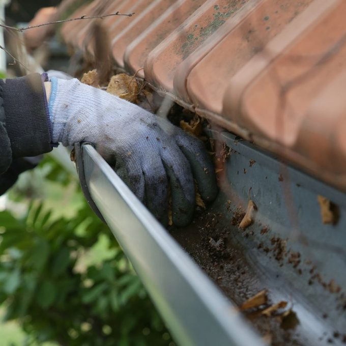 Image of a hand with a work glove cleaning out dirt and leaves from a gutter on a roof