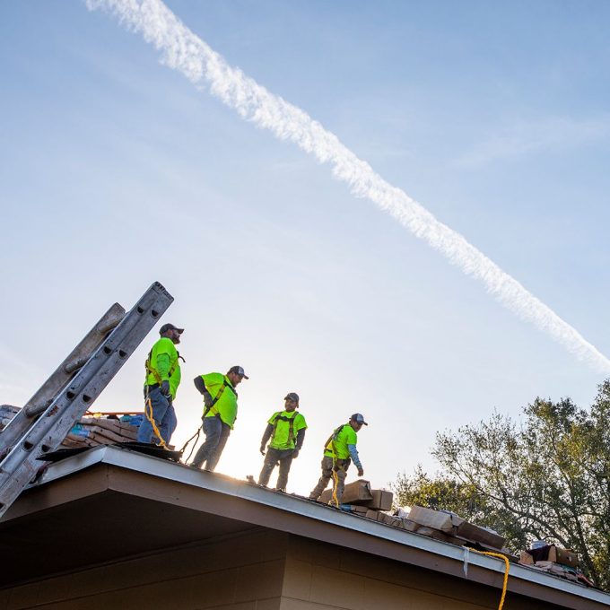 4 roofing contractors on a roof where the photographer is on the ground looking up at the roof